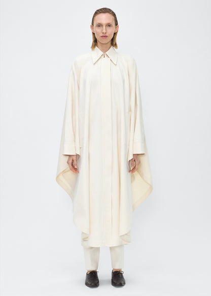 Image of Model facing front, wearing the Langston Poncho, P25914CT, in color ivory, Adam Lippes P25 collection; The Langston Poncho in ivory cotton twill offers an elegant take on the classic poncho. With its modern, relaxed shape, sharp tailoring, and hidden corozo button closure down the center front, it effortlessly elevates any ensemble. The ivory hue and clean lines are complemented by thoughtful details.