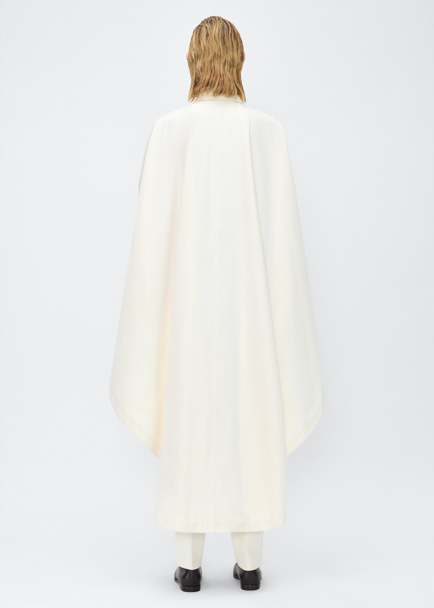 Image of Model facing back, wearing the Langston Poncho, P25914CT, in color ivory, Adam Lippes P25 collection; The Langston Poncho in ivory cotton twill offers an elegant take on the classic poncho. With its modern, relaxed shape, sharp tailoring, and hidden corozo button closure down the center front, it effortlessly elevates any ensemble. The ivory hue and clean lines are complemented by thoughtful details.