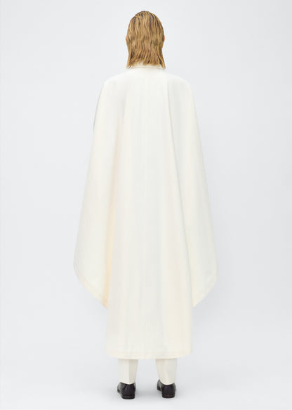 Image of Model facing back, wearing the Langston Poncho, P25914CT, in color ivory, Adam Lippes P25 collection; The Langston Poncho in ivory cotton twill offers an elegant take on the classic poncho. With its modern, relaxed shape, sharp tailoring, and hidden corozo button closure down the center front, it effortlessly elevates any ensemble. The ivory hue and clean lines are complemented by thoughtful details.