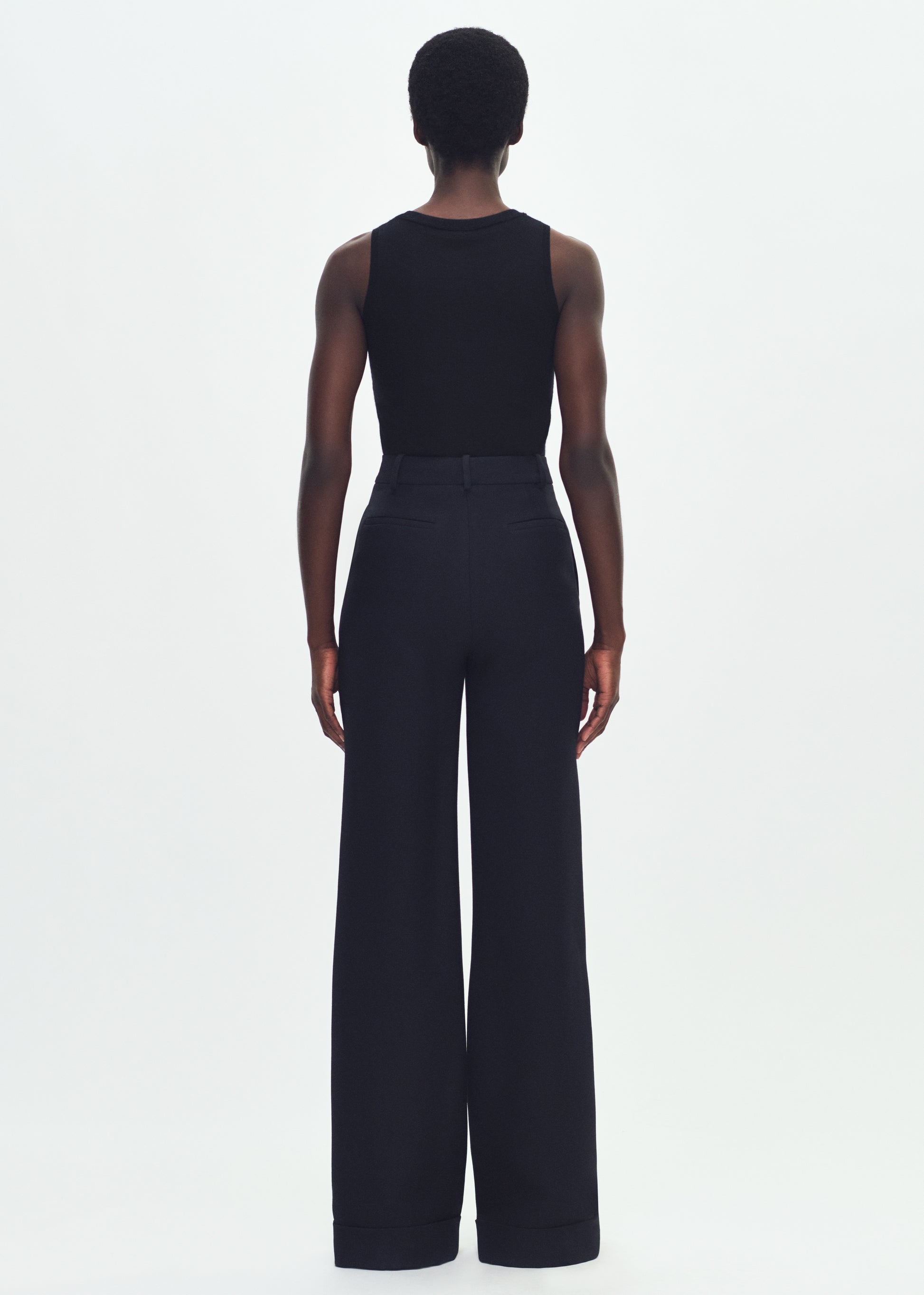 Image of a model facing backward wearing a black sleeveless top tucked into black wide leg pants.