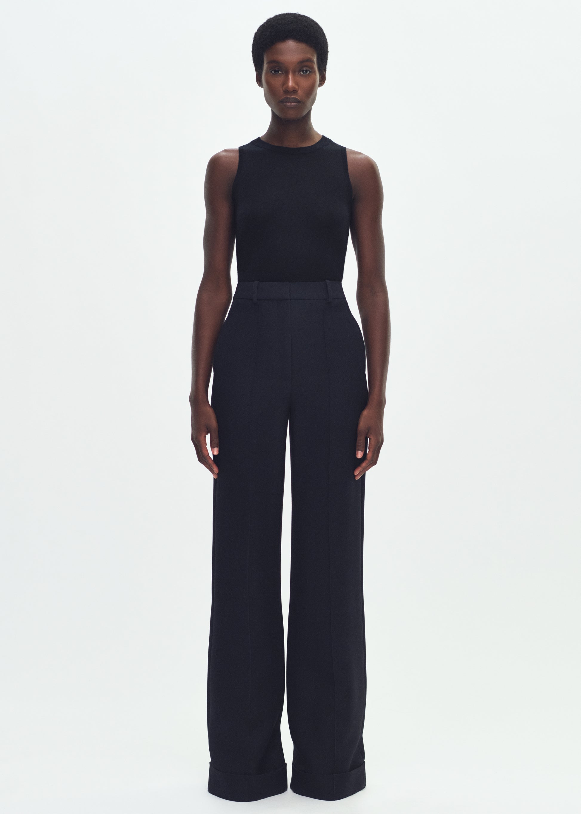 Image of a model facing forward wearing a black sleeveless top tucked into black wide leg pants.