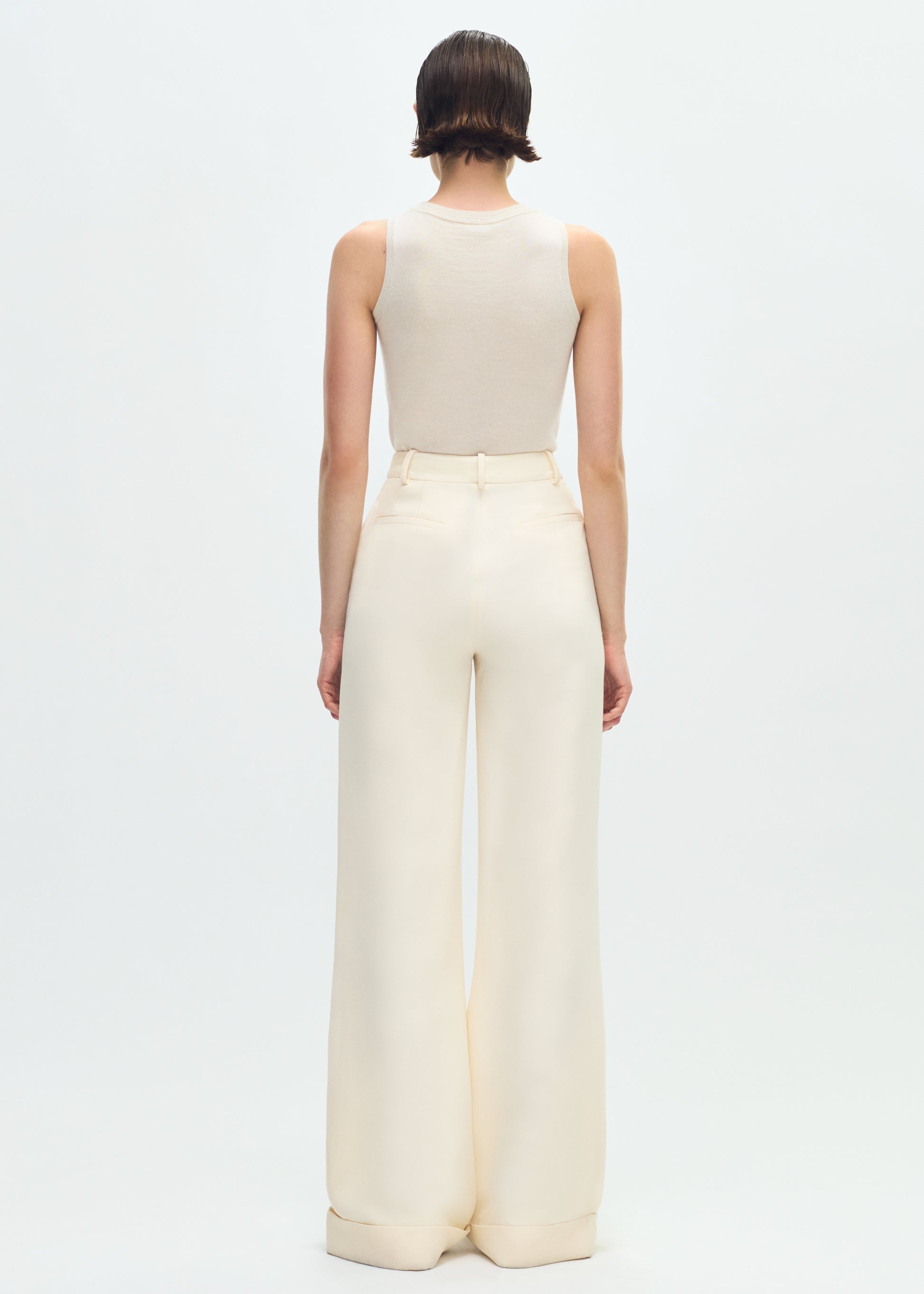 Image of a model facing backwards wearing ivory tank tucked into ivory pants.