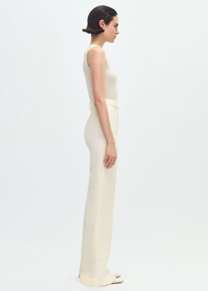 Image of a model facing sideways wearing a white tank tucked into ivory pants.