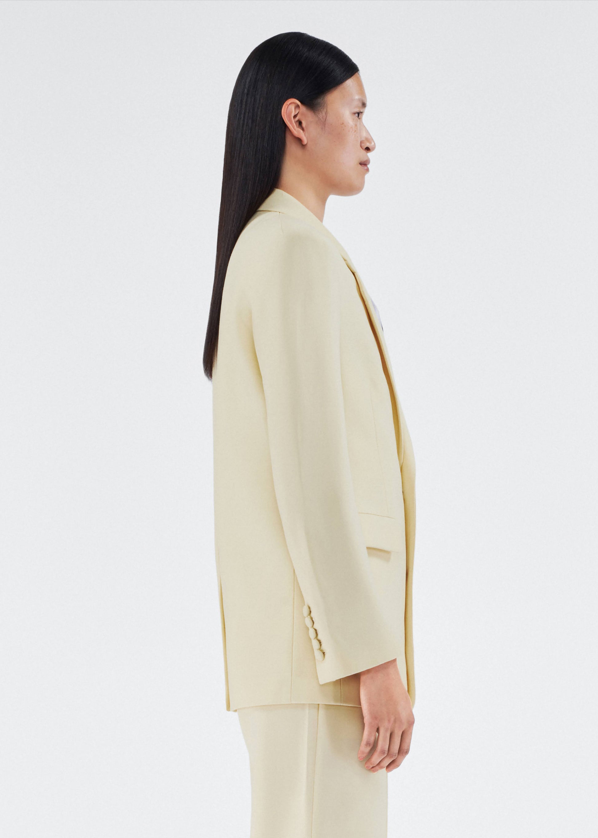 side view of model wearing a classic adam lippes blazer in silk wool rendered in a beurre hue