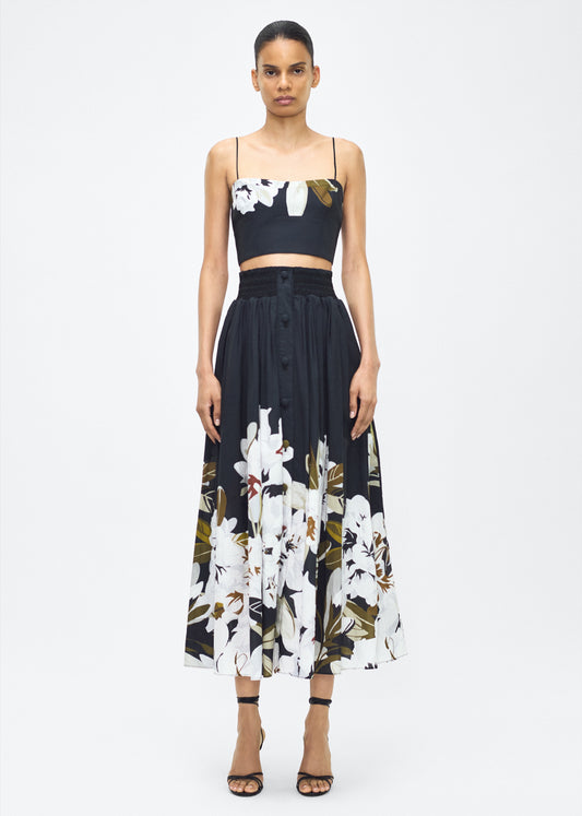 Image of model facing front in the Lovisa Skirt, P25418PV, Black White – Adam Lippes, P25 collection: A signature shape from the atelier, the Lovisa Skirt is crafted from airy printed voile featuring a vibrant Sicily-inspired floral motif. Designed with a smocked waistband for a comfortable fit, the skirt is finished with fabric-covered buttons down the center front. Pair with the Bex Top in Printed Voile for a coordinated look.